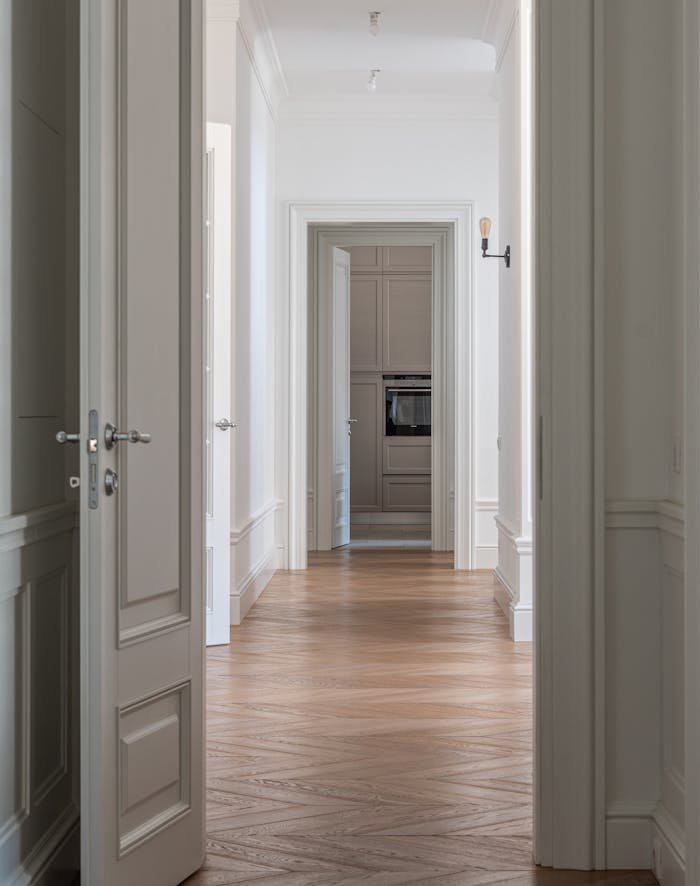 Bright hallway with wooden flooring and white walls leading to a room with built-in cabinets.